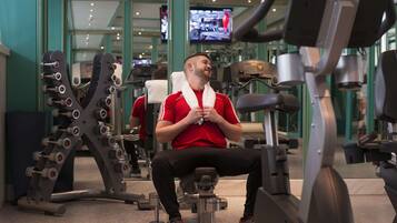 Een fitnessruimte met diverse trainingsapparaten, waaronder een bankdrukapparaat en een rek voor gewichten.