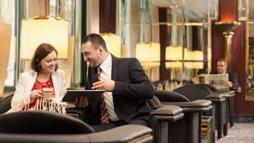 Eine Hotelhalle mit Ledersesseln, einem Couchtisch und einer Person, die eine Zeitung liest.