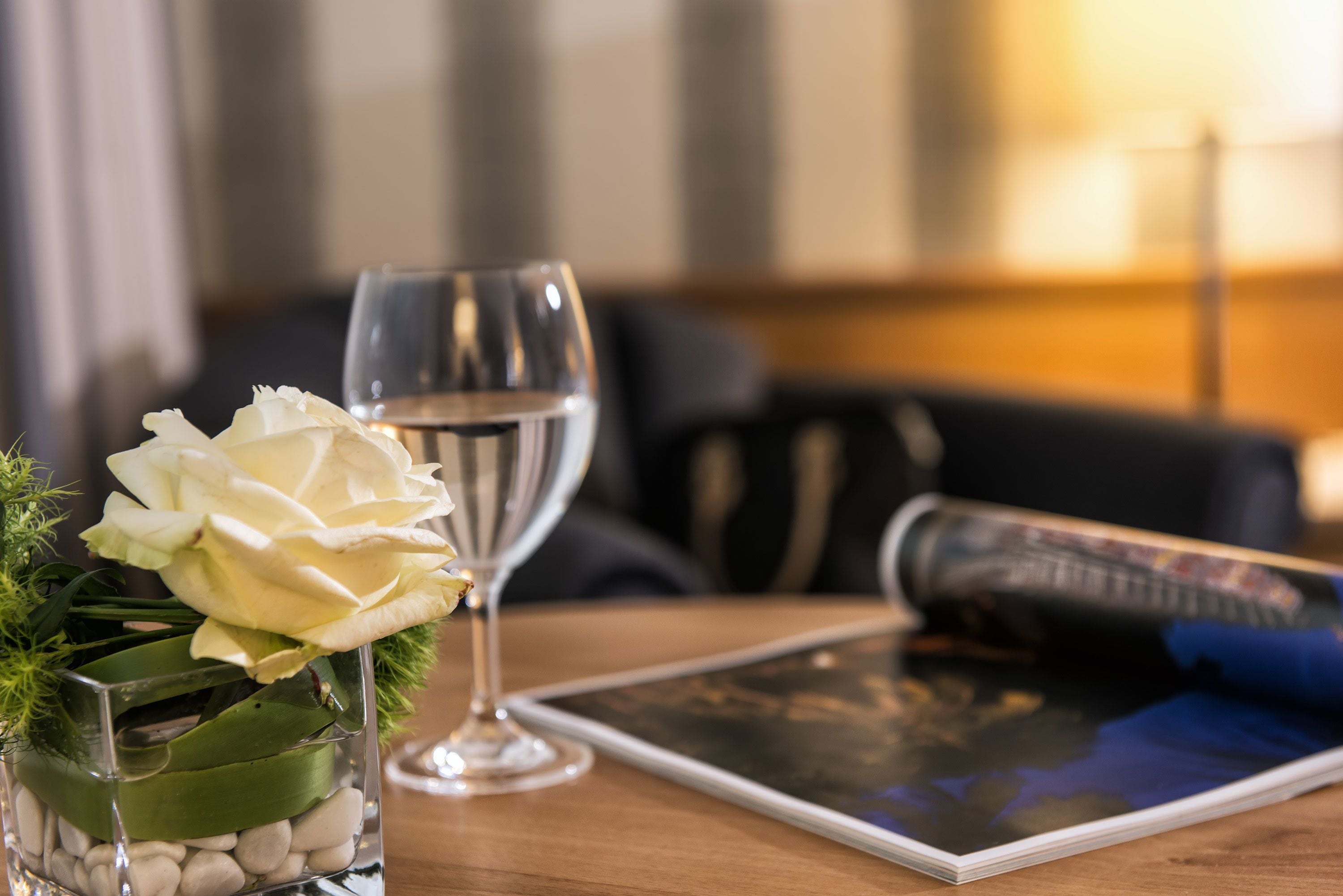 Ein Tablet auf einem Holztisch mit einem Glas Wasser und einer weißen Rose in einer Glasvase.