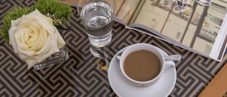 Une table avec un verre d’eau, une tasse de café et une rose blanche dans un vase en verre.