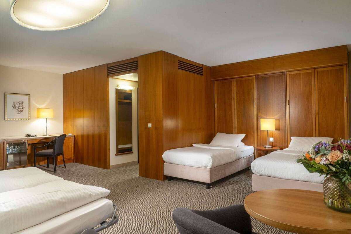 A hotel room with two beds, a desk, a chair, a small table, and a lamp.