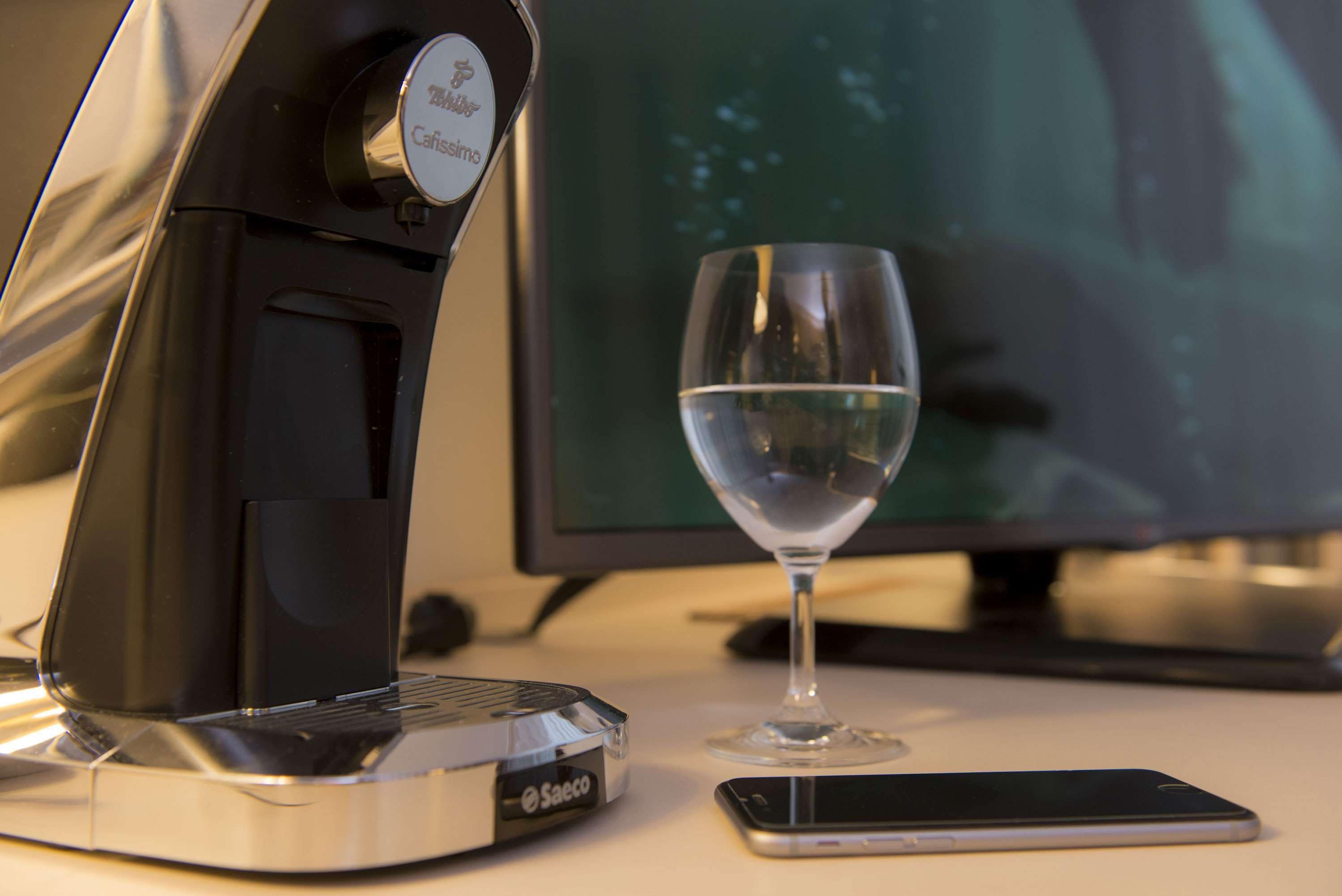 Una cafetera, un vaso de agua y un teléfono inteligente sobre una mesa.