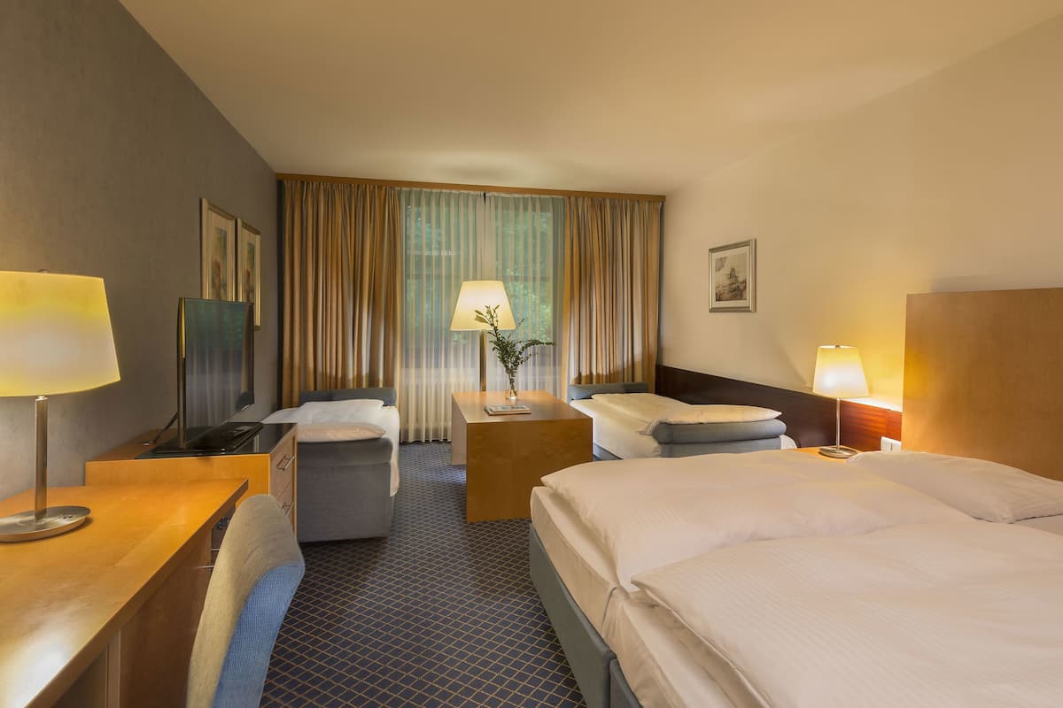 Ein Hotelzimmer mit zwei Betten, einem Schreibtisch, einem Stuhl, einem Fernseher und einem Fenster mit Vorhängen.