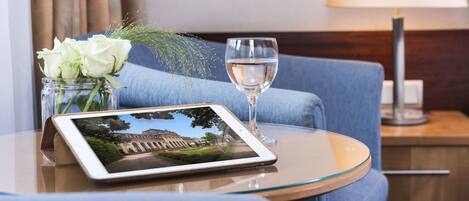 A tablet on a glass table with a glass of water and a vase of white flowers.