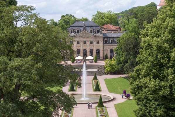 A large historic building with a central fountain, surrounded by well-manicured gardens and trees.
