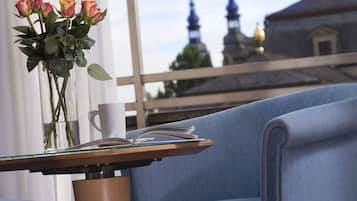 A room with a view of a building with spires, a vase with flowers, a cup, and a book on a table.