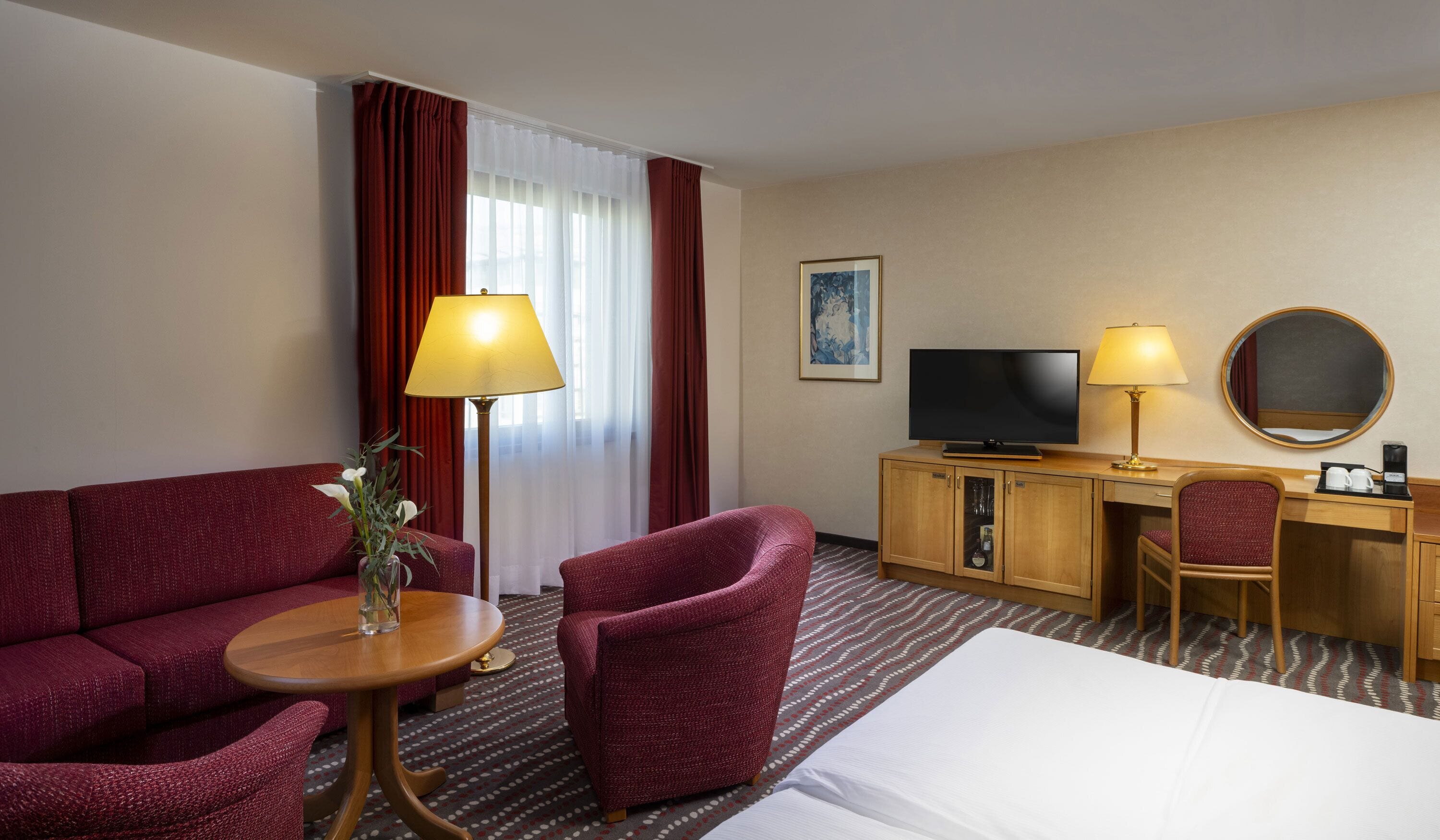 Una habitación de hotel con sofá, sillón, televisor, escritorio y cama.