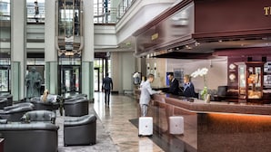 A hotel lobby with a reception desk, seating area, and a large glass window. - Maritim Hotel Magdeburg (Magdeburg)