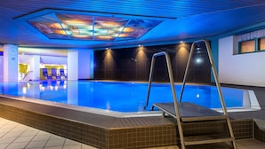 An indoor swimming pool with clear blue water, a tiled floor, and a ceiling with a geometric light fixture. - Maritim Hotel Magdeburg (Magdeburg)