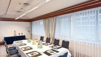 Un salón de conferencias con una larga mesa, sillas, una mesa de buffet y un amplio ventanal con cortinas.