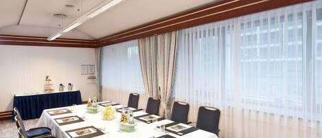 A conference room with a long table, chairs, a buffet table, and a large window with curtains.
