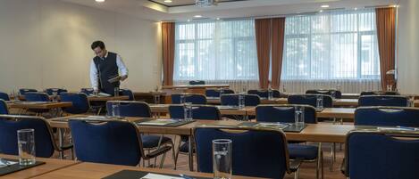 A conference room with rows of tables and chairs, a projector, and a person standing at the front.