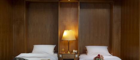 A hotel room with two beds, a nightstand with a lamp, a small table, and a teddy bear on one bed.