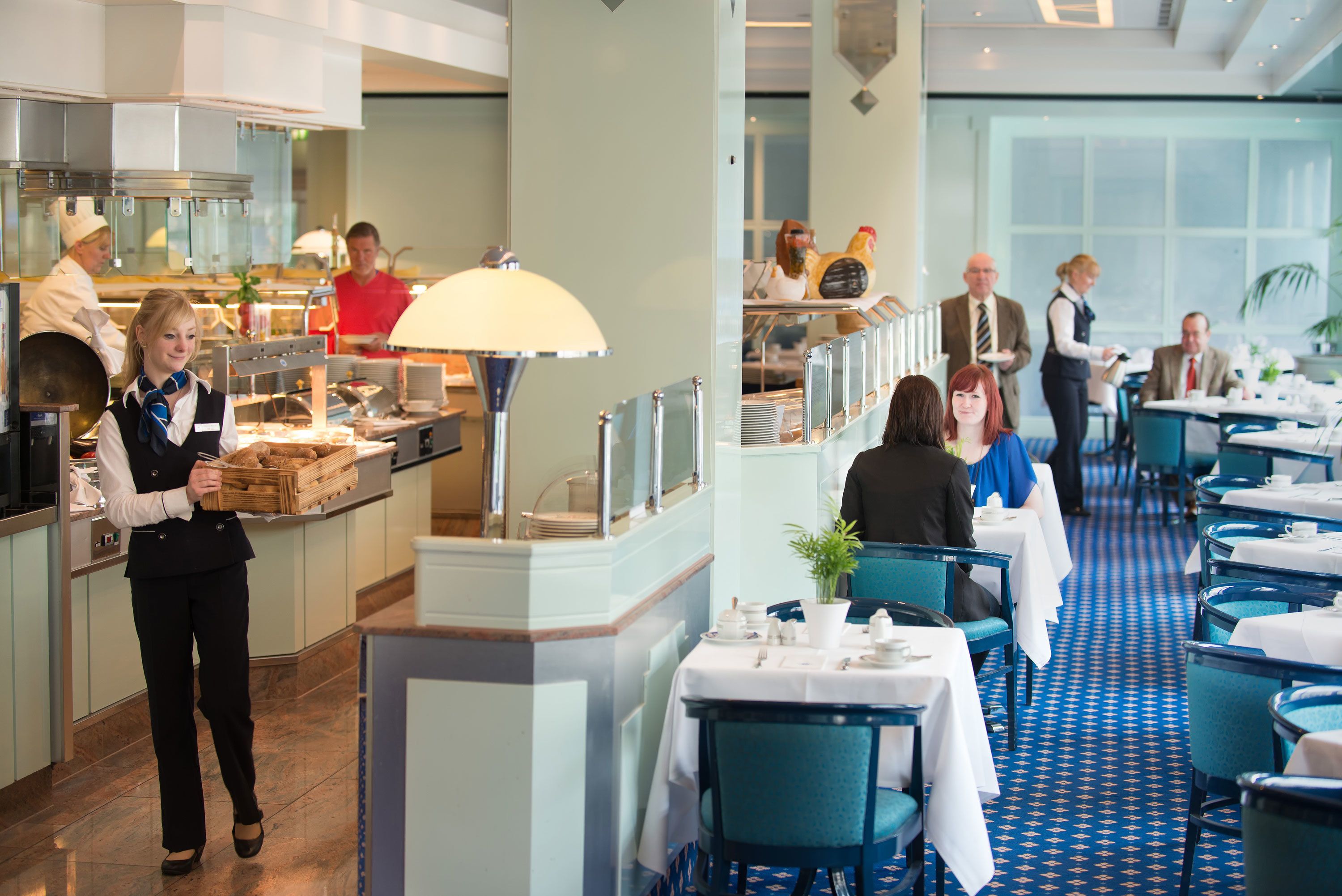 A restaurant with a blue patterned floor, white tablecloths, and a mix of blue and white chairs.