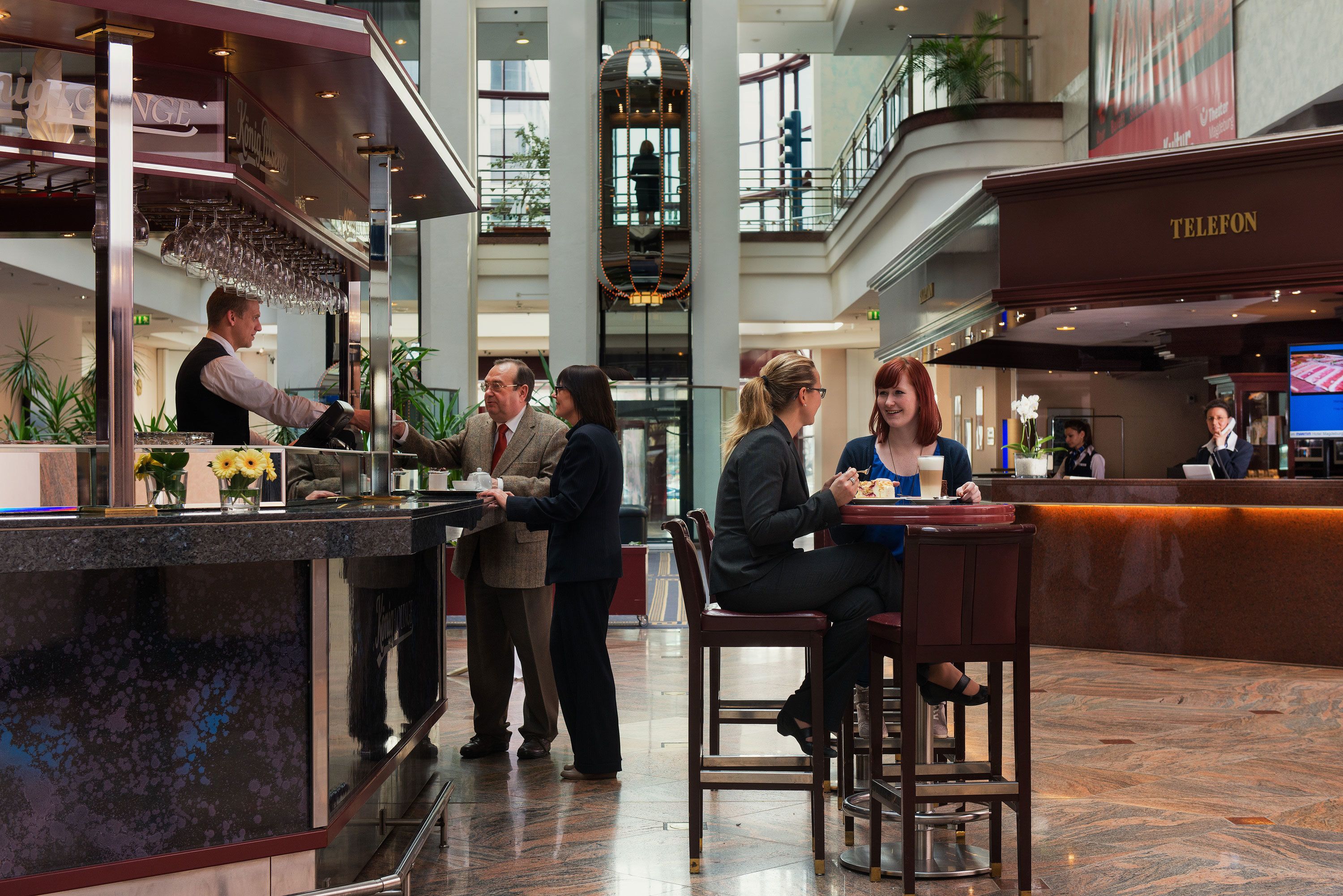 A hotel lobby with a reception desk, a bar area, and a seating area with a high ceiling and modern design.