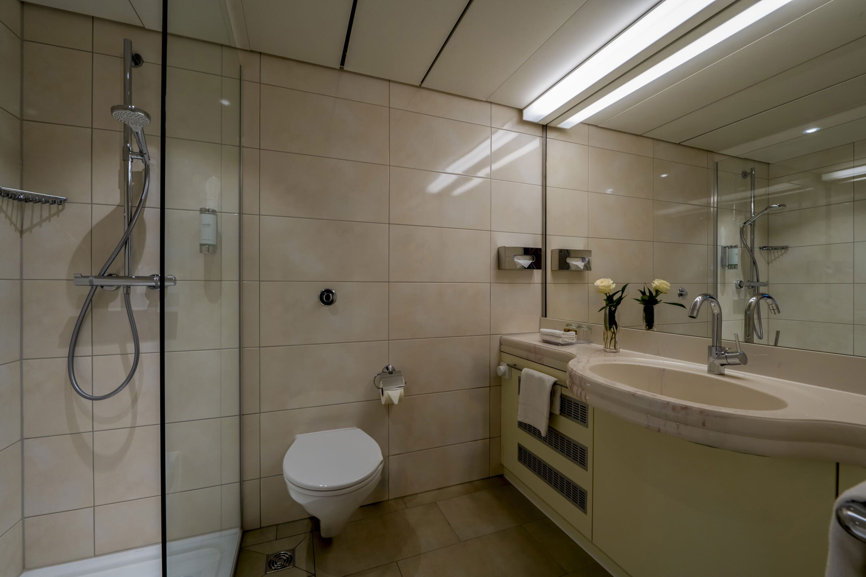 Un baño moderno con cabina de ducha de vidrio, inodoro, lavamanos con espejo y un perchero para toallas.