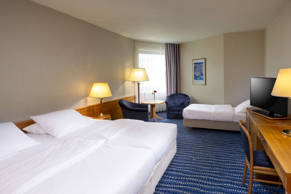 A hotel room with two beds, a desk with a TV, a chair, a small table, and lamps.