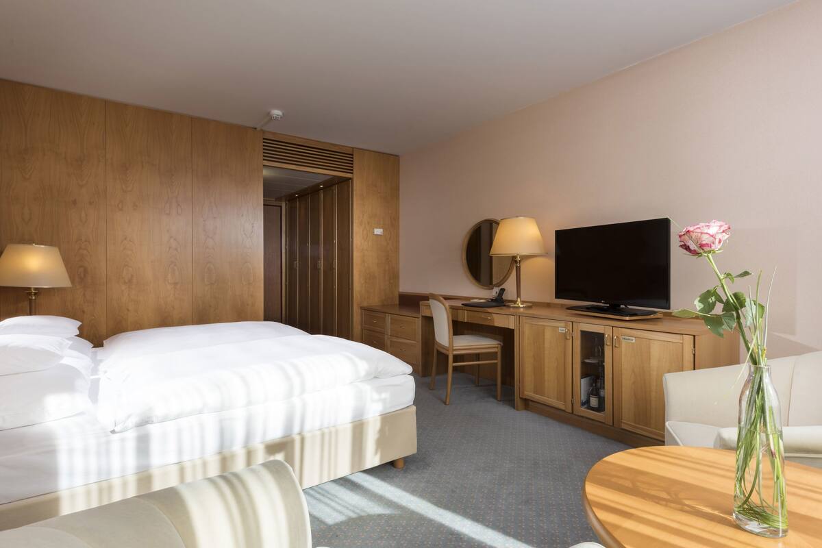 A hotel room with a bed, desk, television, and a vase with a flower.