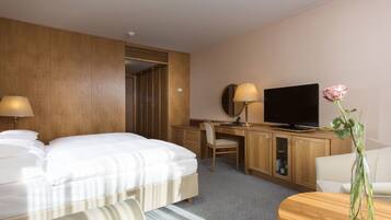 Una habitación de hotel con cama, escritorio, televisor y un florero con una flor.