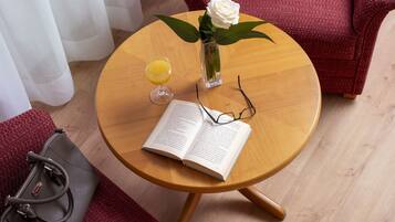 A round wooden table with a book, a glass of orange juice, a vase with a white rose, and a pair of glasses.