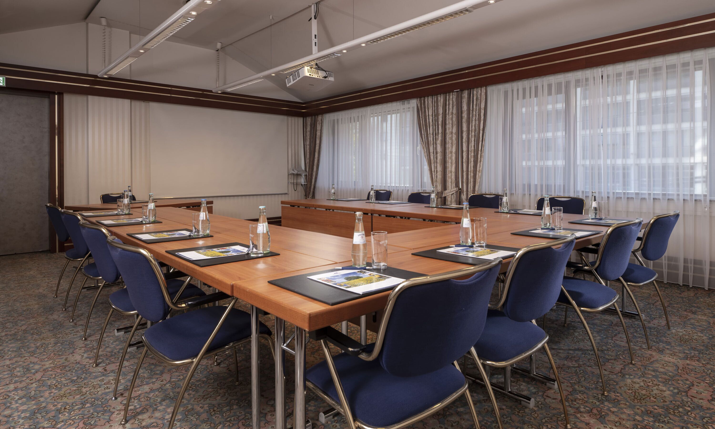 Un salón de conferencias con una larga mesa, sillas azules y un proyector.