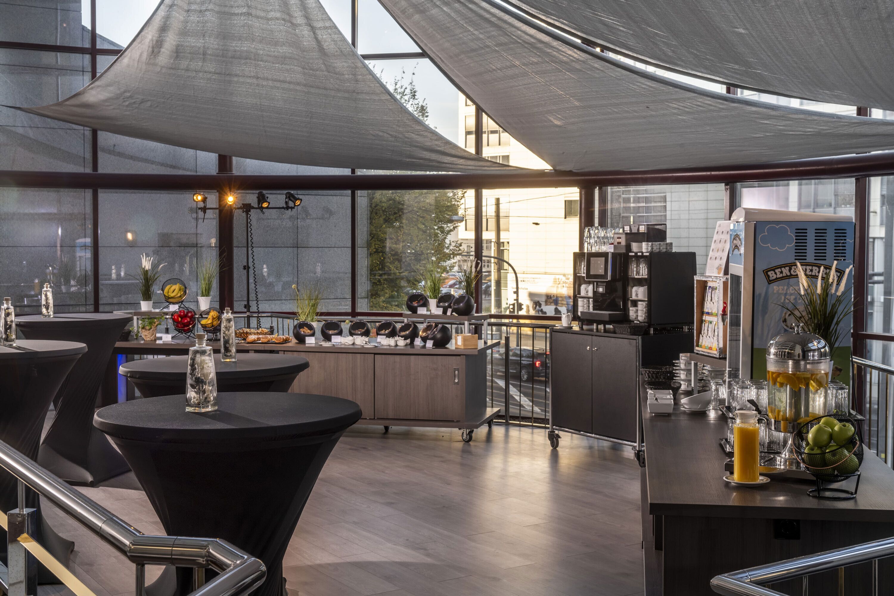 A modern bar area with tables, a beverage dispenser, and a view of the street outside.
