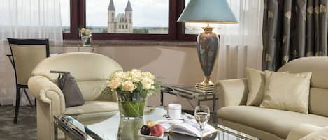A hotel room with a sofa, armchair, and a glass coffee table with a vase of flowers, a book, and a wine glass.