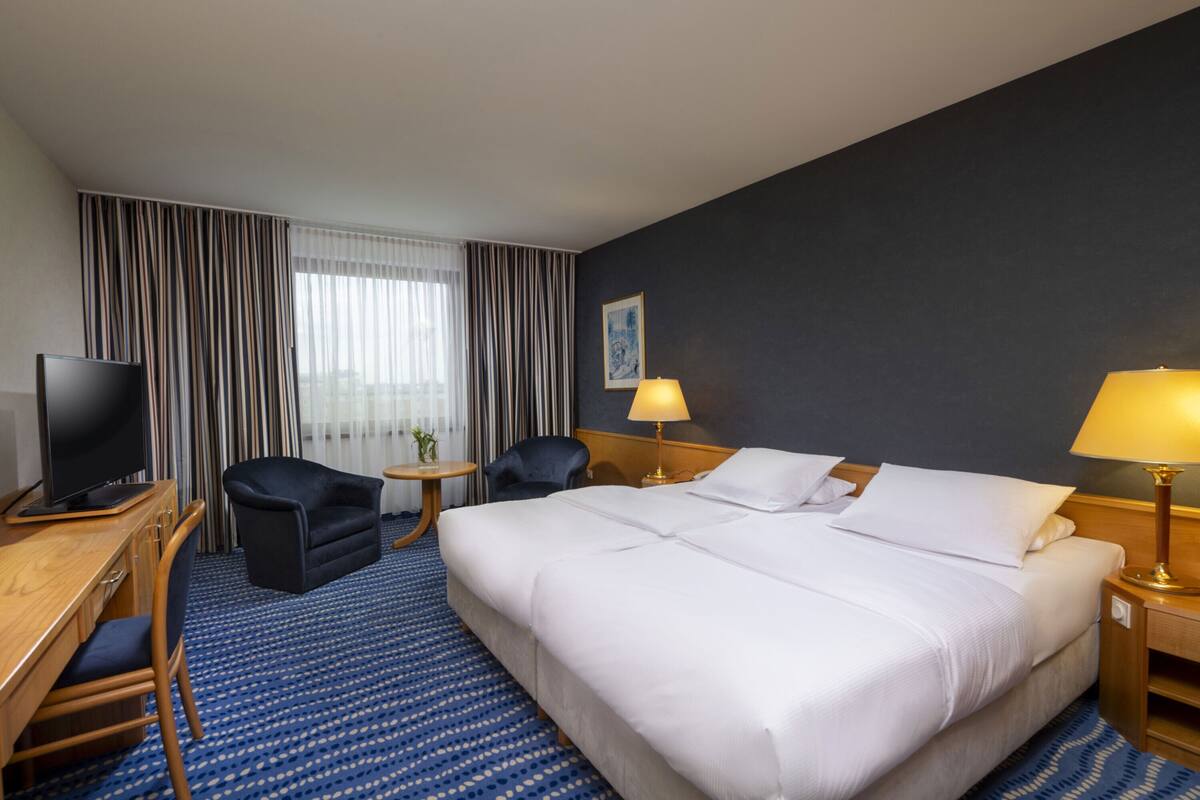 A hotel room with a large bed, a desk with a television, two armchairs, a small table, and a lamp.