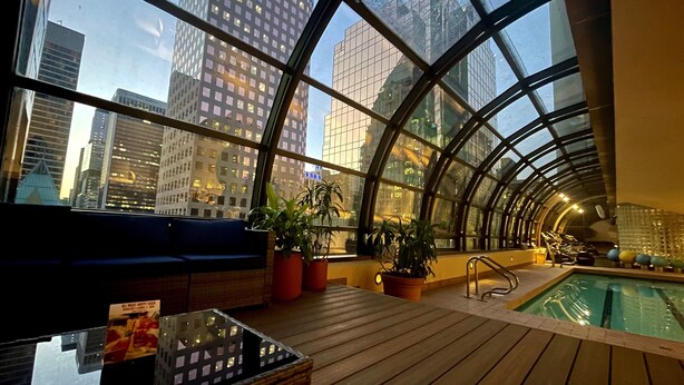A modern indoor pool area with a curved glass ceiling, wooden flooring, and seating areas. - Metropolitan Hotel Vancouver by Marriott (Vancouver)