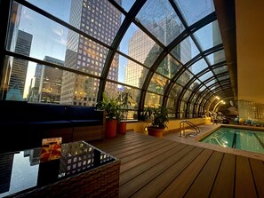 Un espace piscine intérieur moderne, doté d’un plafond incurvé en verre, d’un plancher en bois et de coins salon.