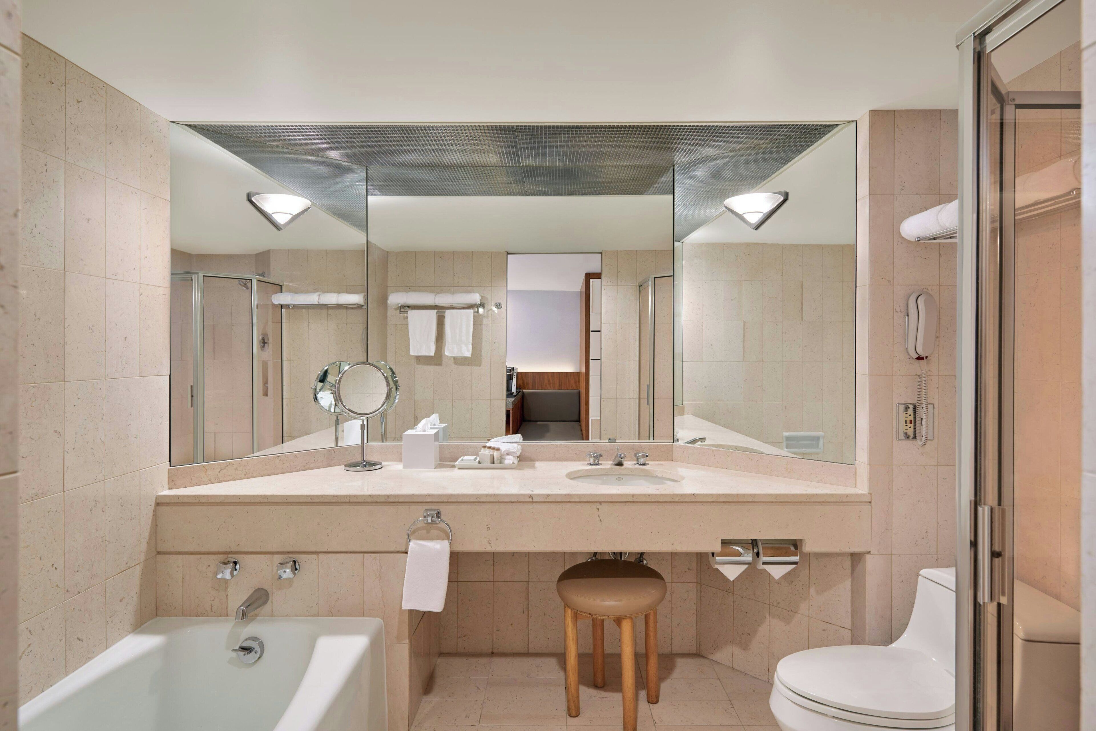 A modern bathroom with a large mirror, a bathtub, a toilet, and a shower area.