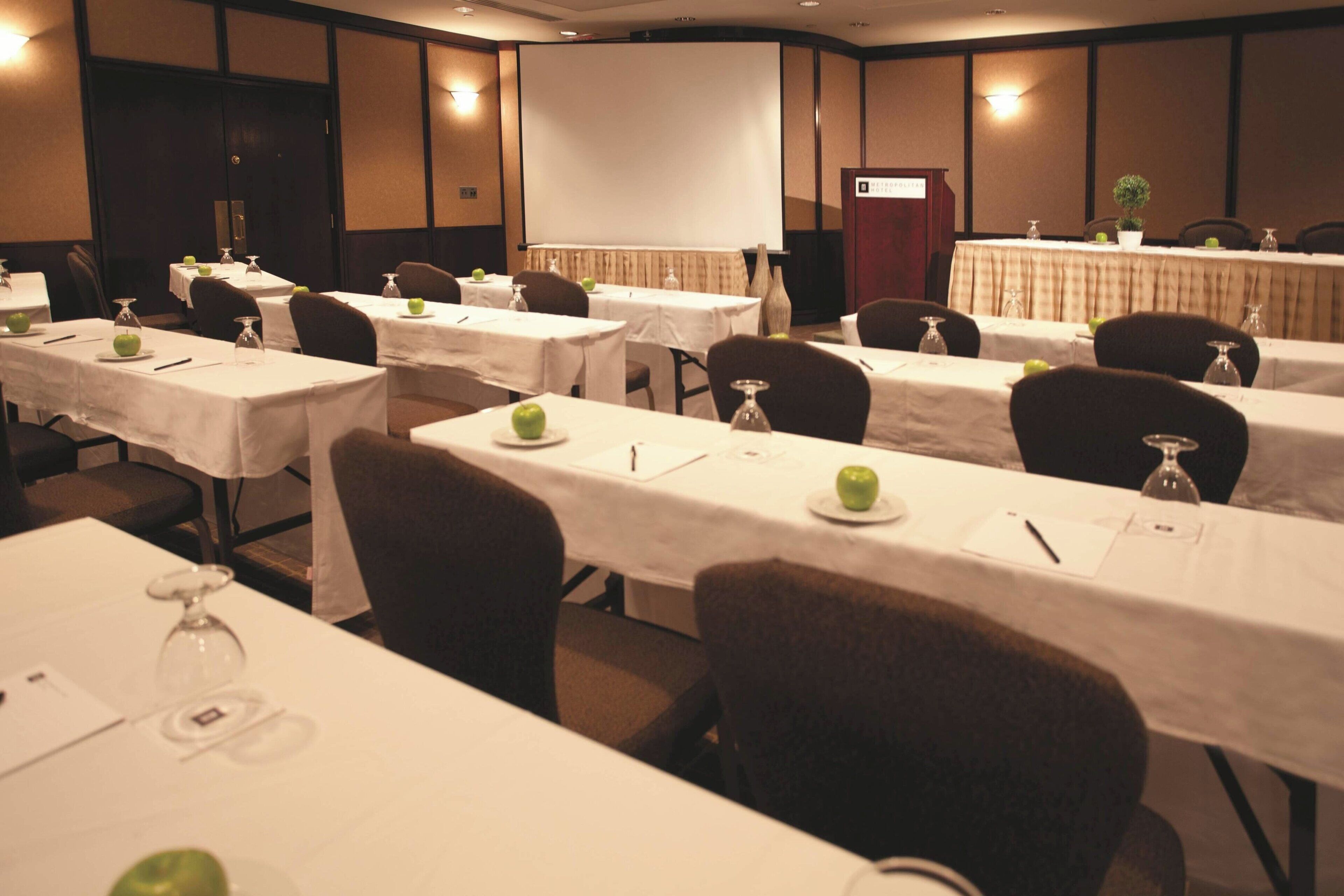 Sala de conferência com várias mesas, cada uma com toalha branca, um copo e uma maçã verde.