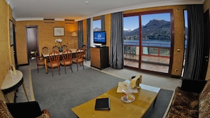 A hotel room with a dining area, a sofa, a television, and a view of mountains and a lake. - Grand Hotel Eden (LUGANO)
