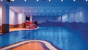 An indoor swimming pool with a tiled floor, red lounge chairs, and a ceiling with recessed lighting. - Grand Hotel Eden (LUGANO)