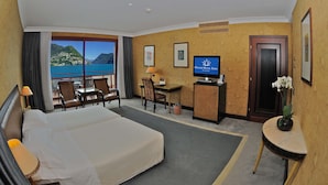 A hotel room with a bed, a desk, a television, and a view of the sea. - Grand Hotel Eden (LUGANO)
