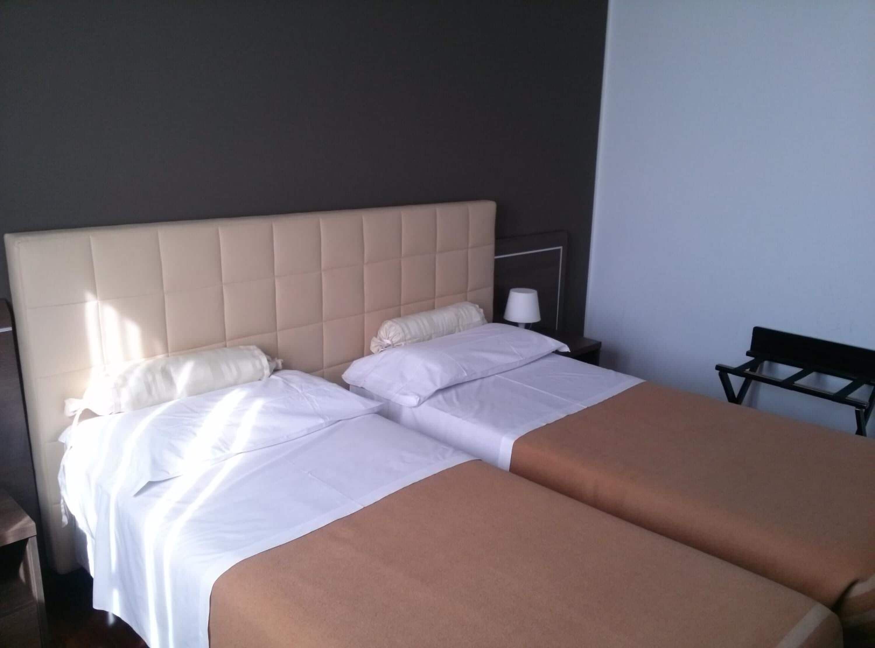 Un lit double avec une tête de lit rembourrée, du linge de lit blanc et une table de chevet avec une lampe.