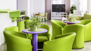 A modern living room with green sofas, a purple table, and a TV in the background. - Hotel Milano Palmanova (Milan)