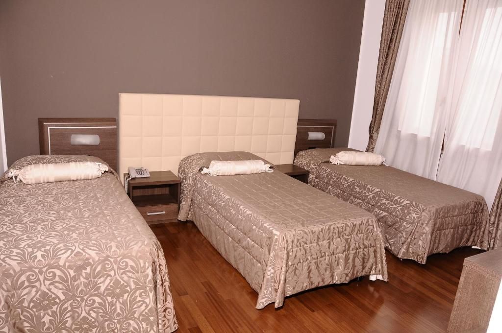 Een hotelkamer met drie eenpersoonsbedden, een houten vloer en een groot raam met gordijnen.