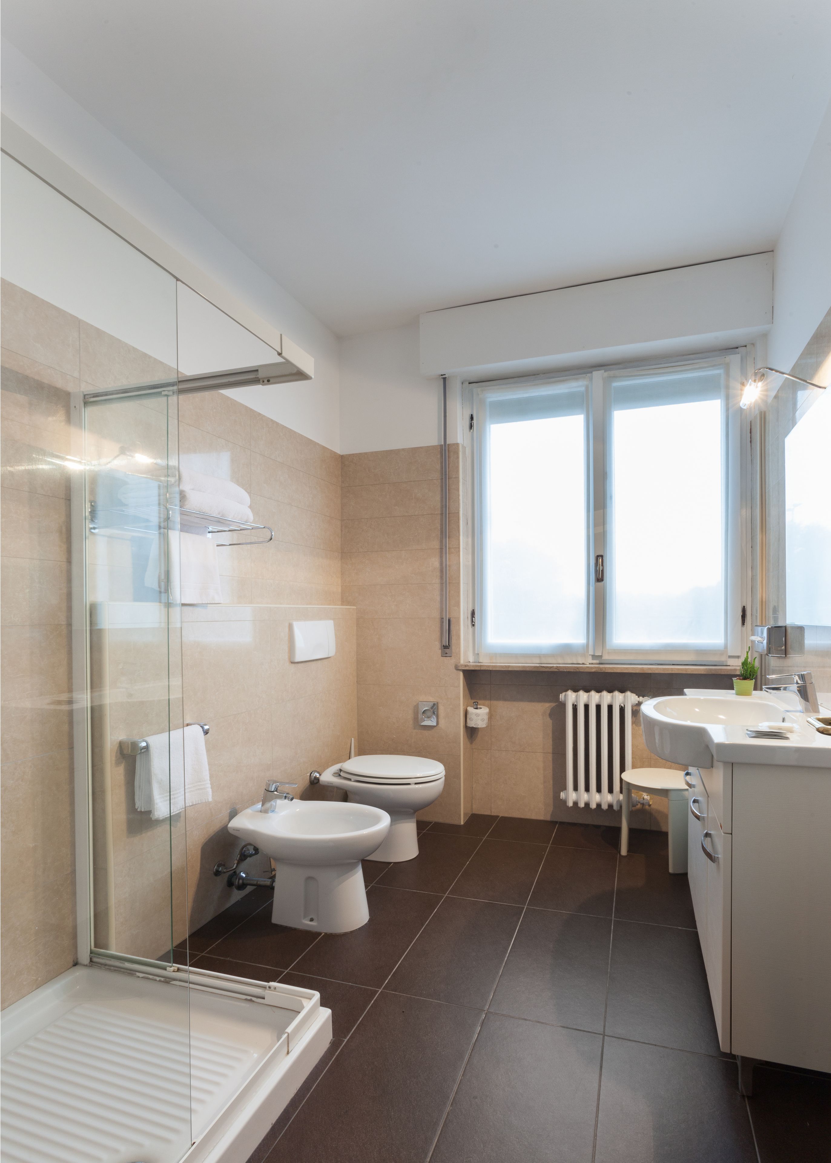 Een moderne badkamer met een douchecabine van glas, twee toiletten, een wastafel en een raam voor natuurlijk licht.