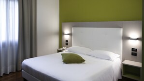 A hotel room with a bed, white bedding, a green pillow, and wall-mounted lights. - Hotel Milano Palmanova (Milan)