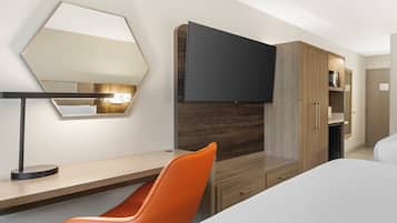 A hotel room with a bed, a desk with a chair, a flat-screen TV, a wardrobe, and a mirror on the wall.
