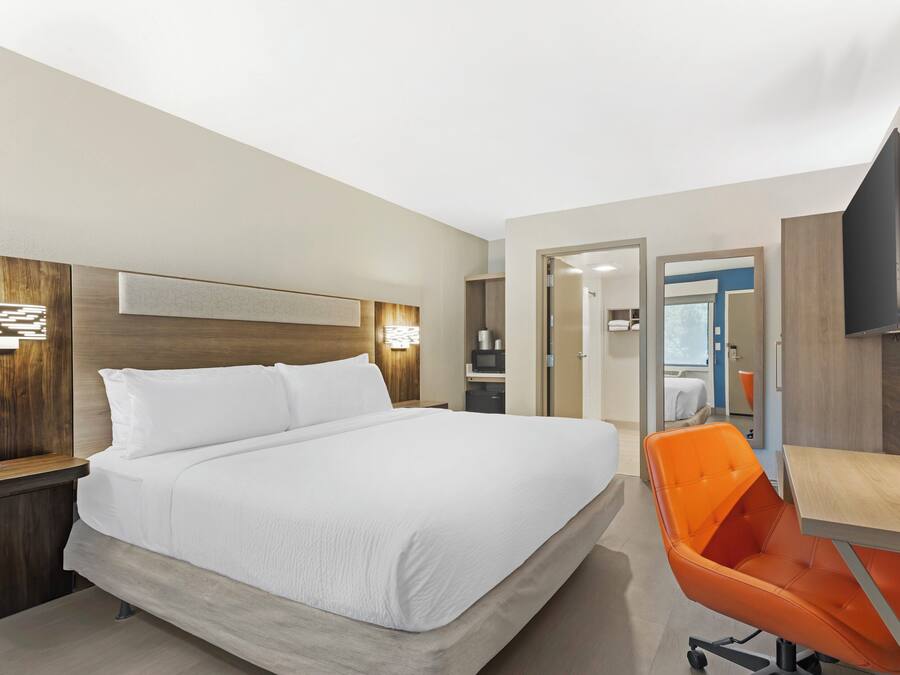 A modern hotel room with a large bed, a desk with a chair, and a television mounted on the wall.