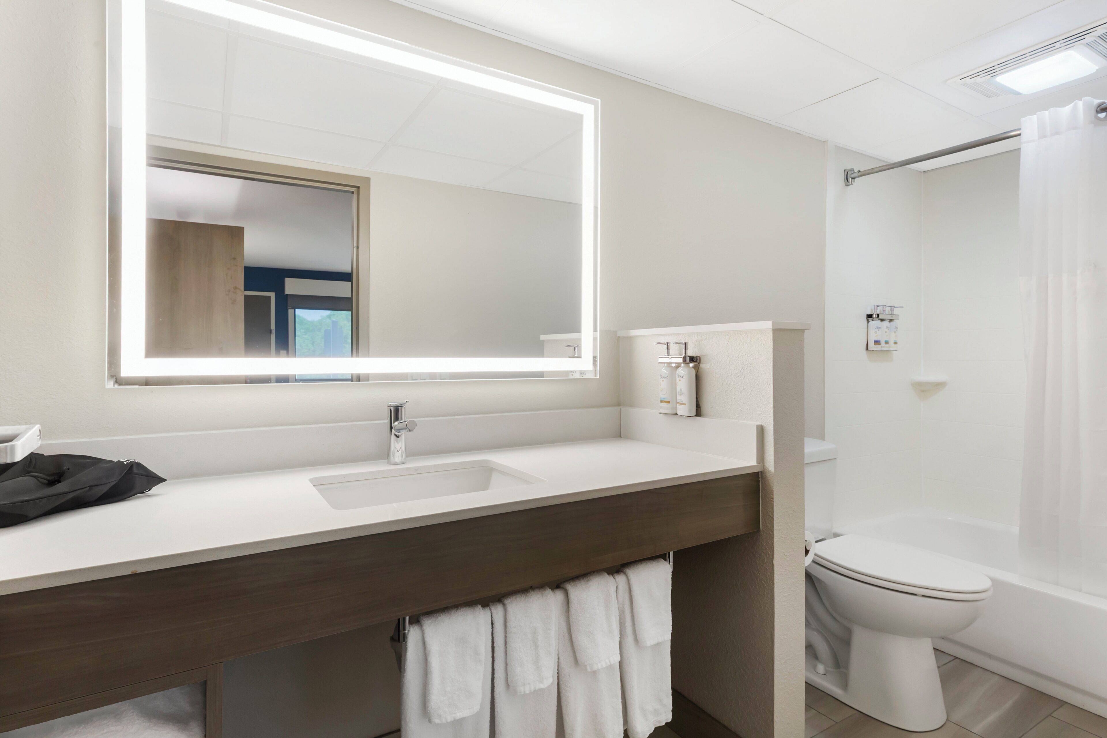 A bathroom with a large mirror, a sink, a toilet, and a shower curtain.