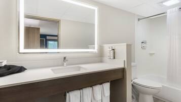 A bathroom with a large mirror, a sink, a toilet, and a shower curtain.