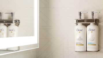A modern bathroom with a chrome faucet, a large mirror, and two Dove hand soap dispensers mounted on the wall.
