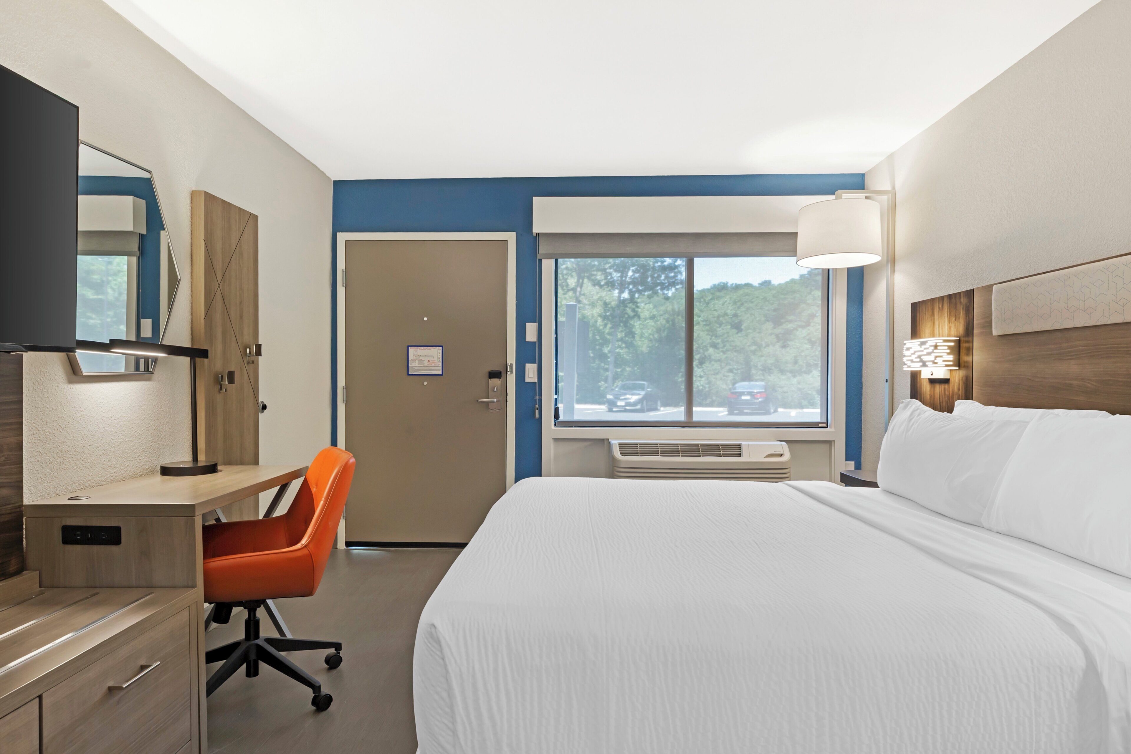 A hotel room with a bed, desk, chair, window, and a view of the outside.