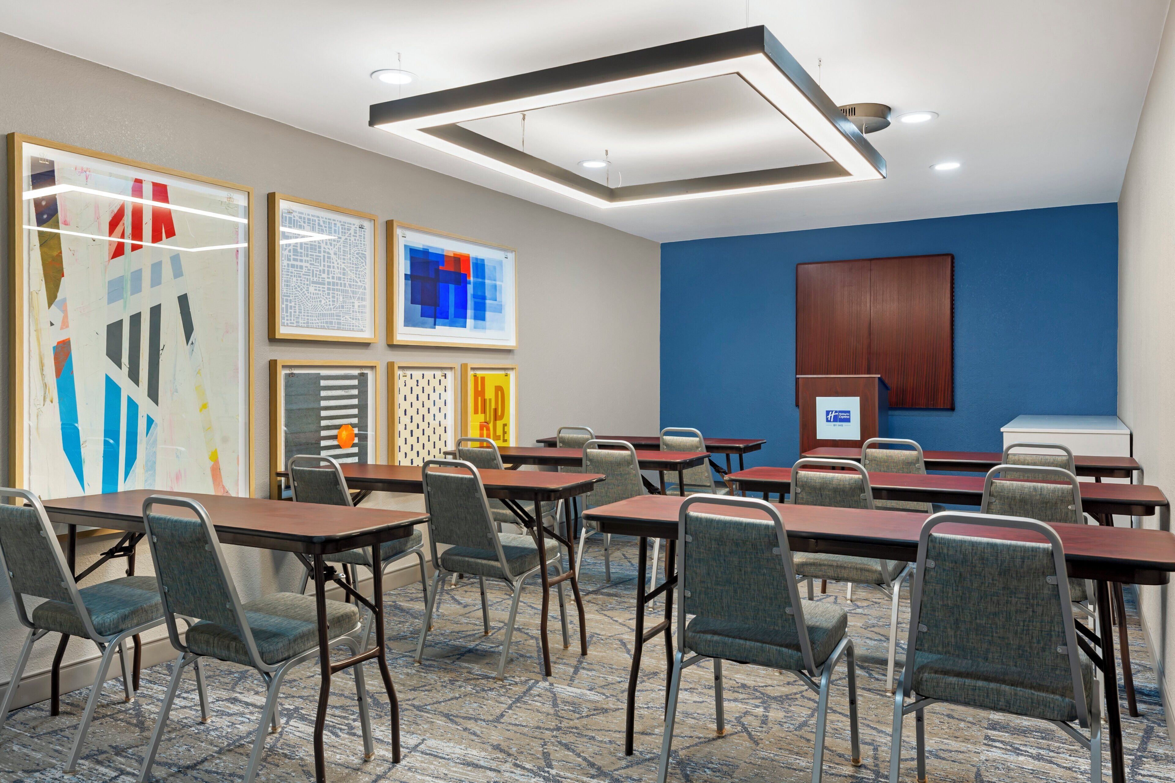 Une salle de conférence équipée de tables et de chaises, avec un mur d’accent bleu et des œuvres d’art encadrées.