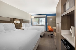 A hotel room with two beds, a desk, an orange chair, and a view of the outdoors.