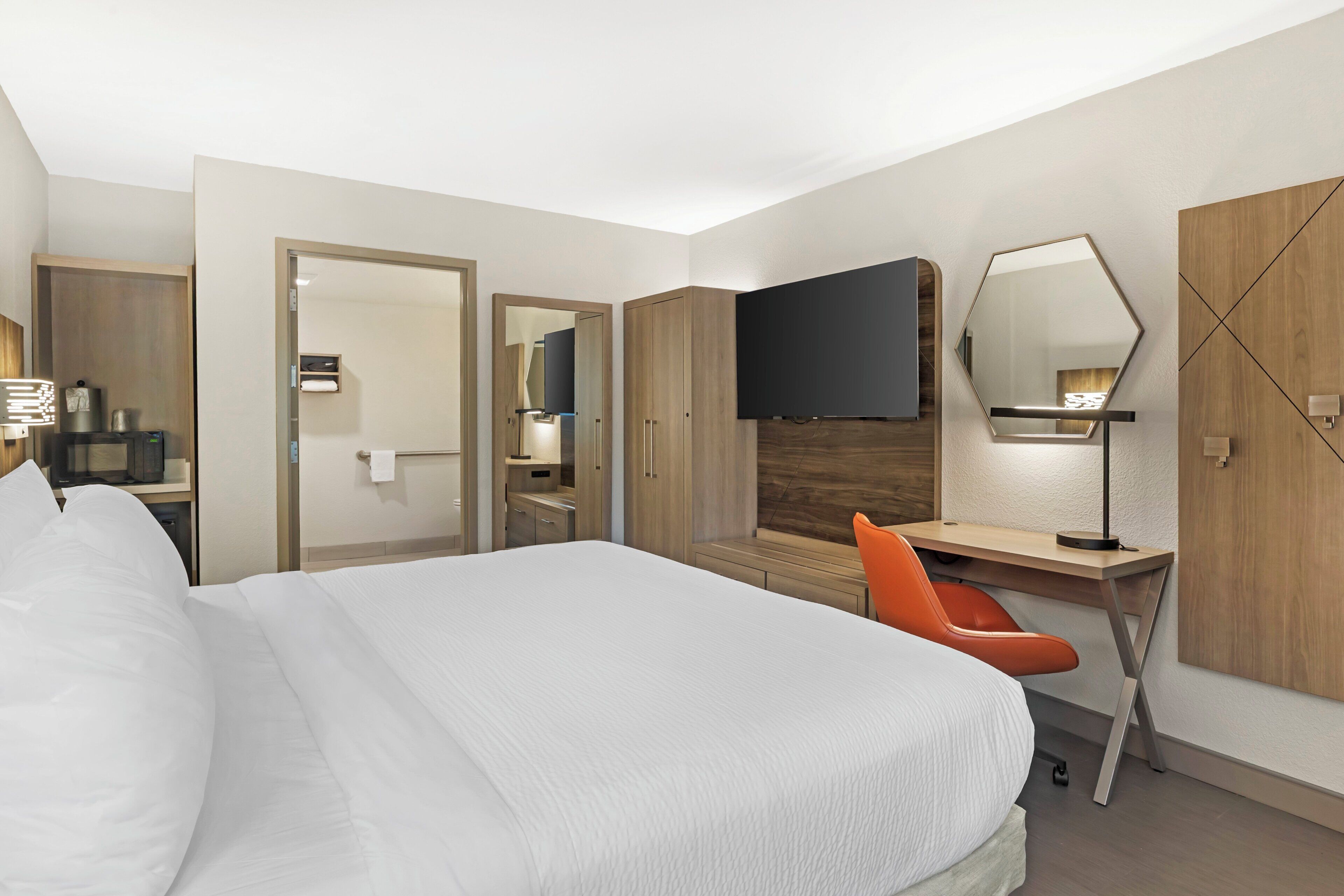 Une chambre d’hôtel avec un grand lit, un bureau avec une chaise, un téléviseur à écran plat, un miroir et une armoire.