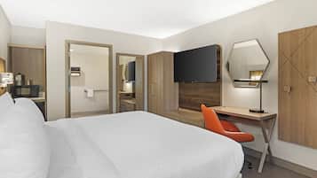 Une chambre d’hôtel avec un grand lit, un bureau avec une chaise, un téléviseur à écran plat, un miroir et une armoire.